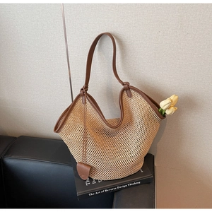 Detail of straw tote bag with brown leather trim and heart charm on a black sofa
