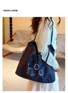 Detail view of deep blue denim tote bag with white embroidery and shoulder straps