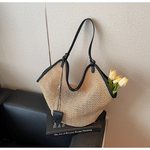 Detail of hand-woven straw tote bag with black leather handles and hollow mesh pattern