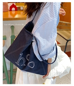 Detailed view of dark blue denim tote bag featuring white letter embroidery and contrast stitching
