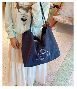 Detailed view of dark blue denim tote bag with white letter print and rope handles