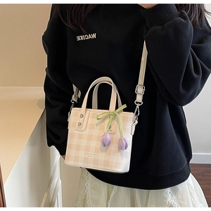 Detail of cream checkerboard crossbody bag with tulip charm and green ribbon detail