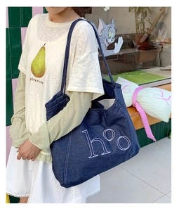 Detailed close-up of dark blue denim tote bag with white h°o embroidery in outdoor setting