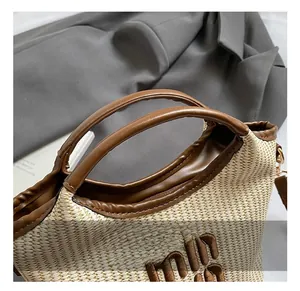 Close-up of woven straw tote bag with brown leather handles and embroidered logo detail