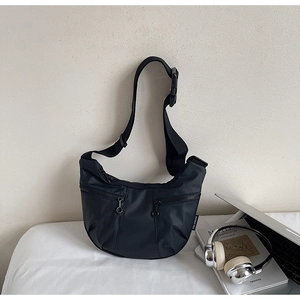 Detail of black nylon half-moon crossbody bag with silver laptop and art magazine
