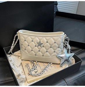 Close-up of quilted cream crossbody bag with silver star charms in luxury gift box