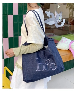 Detail of deep blue denim tote bag with h°o embroidery being worn over the shoulder