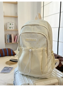 Detail view of beige star print backpack featuring soft plush logo and drawstring front pocket