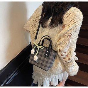 Close-up of gray checkered crossbody bag featuring tulip pendants and a bow accessory