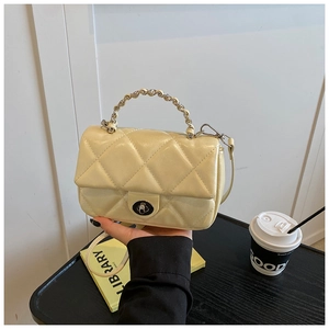 Detail of light yellow quilted mini bag with metal chain handle and oval turn-lock closure