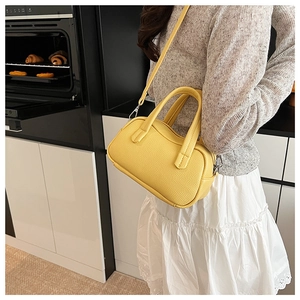 Sac Boston en cuir jaune à motif litchi porté par un mannequin dans un décor de cuisine