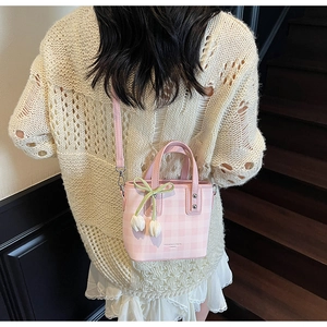 Pink checkered bucket bag with flower charm shown in a stylish crossbody carry style