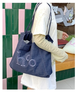 Detail of blue denim tote bag with white h'o print and sturdy shoulder straps