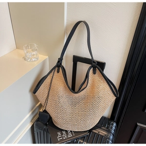 Détail du grand sac cabas en paille tissée avec anses en cuir noir sur une valise