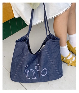 Close-up of deep blue denim tote bag with white letter embroidery and stitching detail