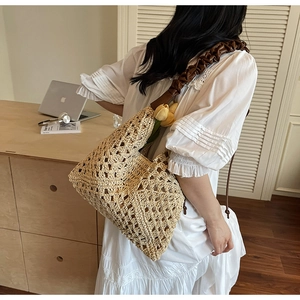 Detail of hand-woven straw beach tote with brown pleated faux leather shoulder strap