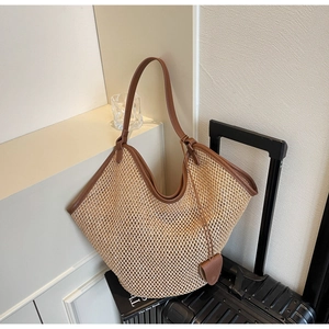 Détail d'un sac cabas en paille tressé avec bordure en cuir marron et breloque cœur