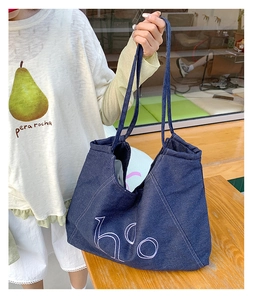 Detailed view of dark blue denim tote bag featuring white hoo letter art and stitching