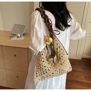 Detail of hollow woven straw beach bag with dark brown ruched strap and tulip decoration