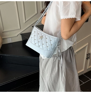 Detail of light blue quilted shoulder bag with star charm and silver chain strap on model