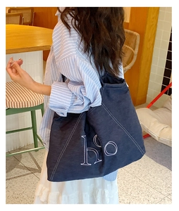 Detail of blue denim tote bag with white ho embroidery and contrast stitching on shoulder