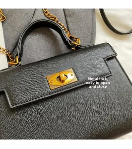 Detail of black cross-grain leather handbag with golden twist lock and metal chain