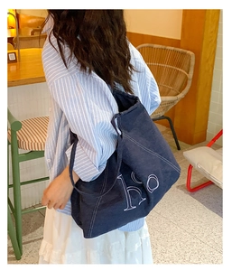 Side view of a large navy denim tote bag with white contrast stitching and ho logo print