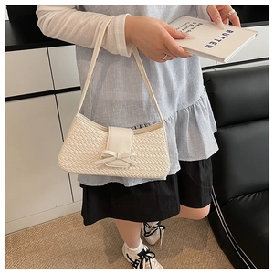 Close-up of cream woven shoulder bag with a leather bow detail and sleek underarm strap