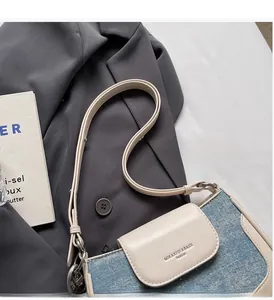Detailed view of blue denim and white leather crossbody bag on a grey blazer garment