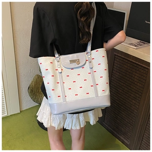 Detail of grey tote bag with red bow pattern featuring metal plate and heart charm