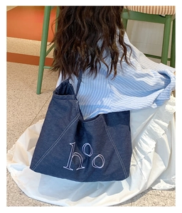 Deep blue denim tote bag with hOo embroidery shown on model sitting on a green stool