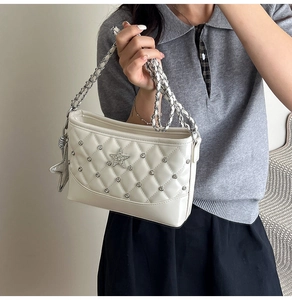 Detail of white quilted bucket bag with silver star studs and metal chain strap