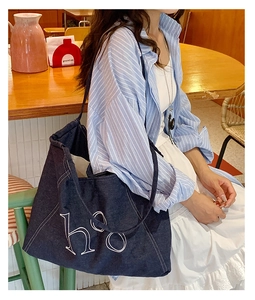 Detail of a large blue denim tote bag with heo white embroidery and shoulder strap