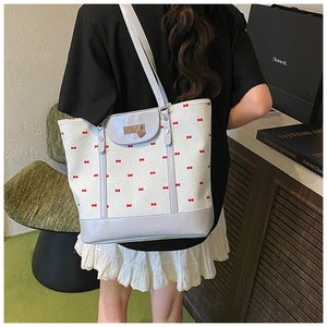 Detail of white tote bag with red bow prints and a heart-shaped metal charm accessory