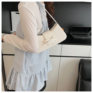 Detail of cream woven shoulder bag featuring a leather bow flap and braided texture