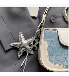Detail of silver starfish and balloon dog charms on a white and denim leather bag