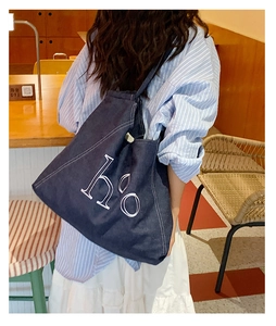 Detail of blue denim tote bag with white embroidery and stitching on shoulder strap