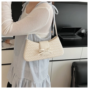 Detail of cream woven shoulder bag with bow accent worn in a workplace setting