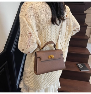 Detail of dark brown lychee leather bag featuring golden twist lock and chain strap