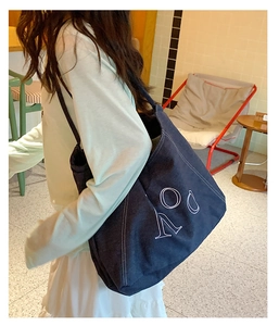 Detail of a navy blue denim tote bag with white LOV embroidery on the shoulder