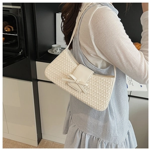 Close-up of white woven underarm bag with leather bow detail on model in lifestyle setting