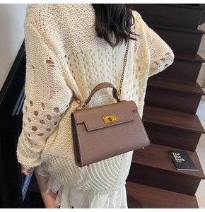 Detail of tan leather handbag with gold twist lock and chain strap on a model