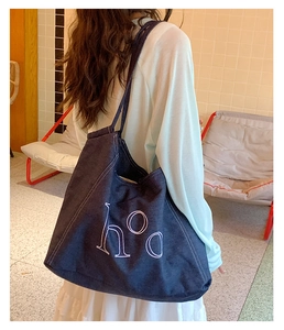 Detail of dark blue denim tote bag with white 'hoo' lettering and stitching