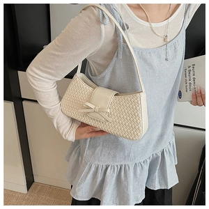 Detail of white woven underarm bag featuring a leather bow accent on a model