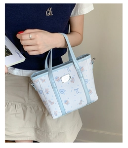 Detail of light blue cartoon bear print tote bag with silver logo plaque and metal rings