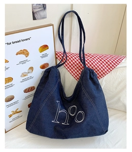 Detail of navy denim tote bag with white letter embroidery and a drawstring closure