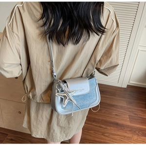 Detail of silver flap and blue denim crossbody bag with large star pendant on model