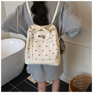 Detail of a creamy white backpack with red bow prints and a silver heart pendant lock