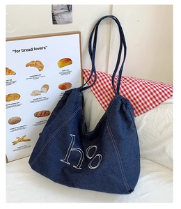 Detail of navy denim tote bag with white H8 embroidery on soft fabric surface