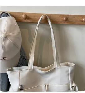Detail of white canvas tote bag with long handles and side pocket on a wooden hook